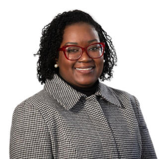 Professional photo of a smiling woman with short curly hair and red glasses.